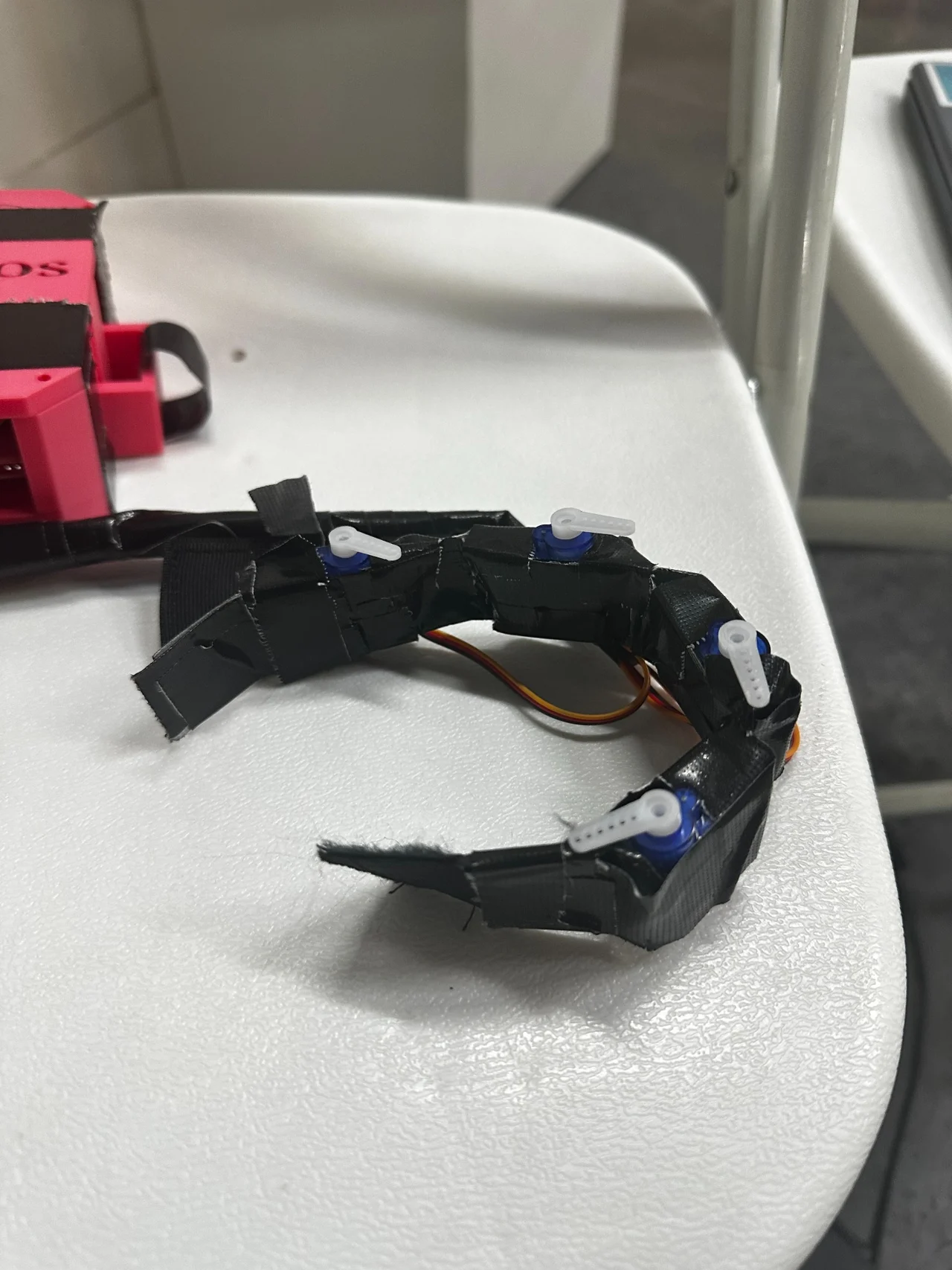 Close-up of the wearable hardware’s curved black band, blue servo actuators, white actuator arms, and wiring.